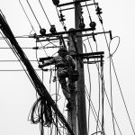 grayscale photo of person climbing electric post