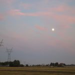 the sun is setting over a field with power lines