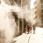 People walk down a sunny street with misting spray.