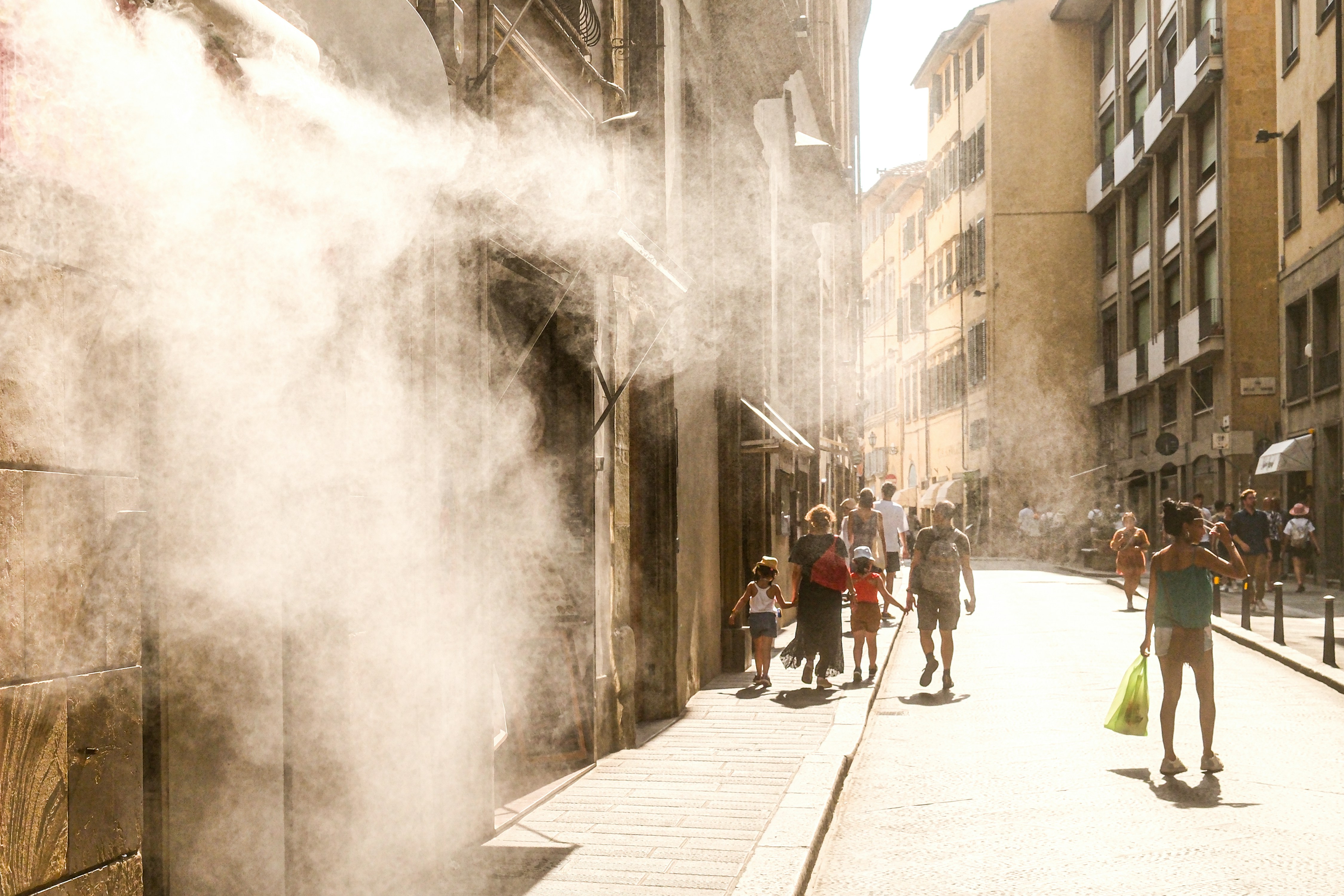 People walk down a sunny street with misting spray.