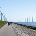 Wind turbines stand in a line along the coast.