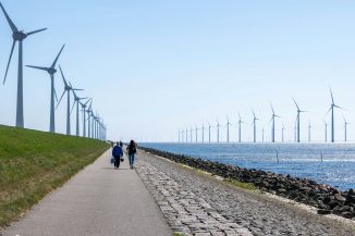 Wind turbines stand in a line along the coast.