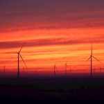 Wind turbines silhouetted against a vibrant sunset sky