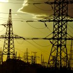 Power lines stand against a yellow sky.