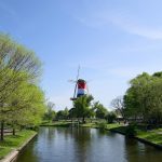 Dutch windmill on a canal with green trees.