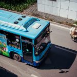A blue bus drives down a street with a motorcycle.