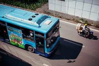 A blue bus drives down a street with a motorcycle.