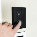 Finger pressing button on digital thermostat display.
