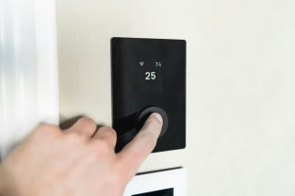 Finger pressing button on digital thermostat display.